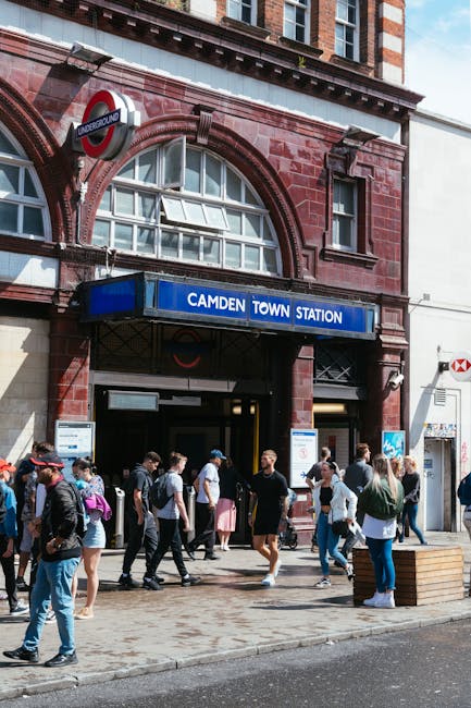 A busy street scene in Camden Town, North London, featuring a corner building with a white façade and large windows, housing a pub called 'The World's End'. In the foreground, a pedestrian traffic li